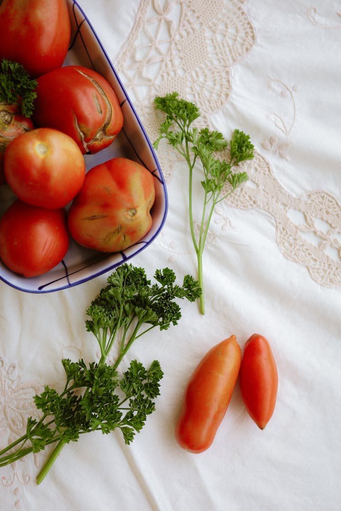 A flat lay of fresh tomatoes and herbs elegantly arranged on a lace tablecloth, perfect for culinary themes.